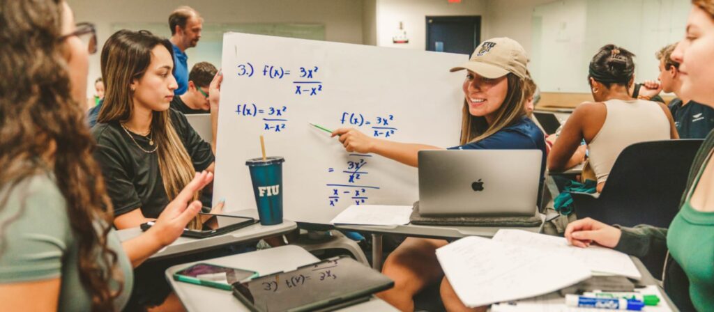 Female FIU student showing whiteboard with calculus work to her peers.